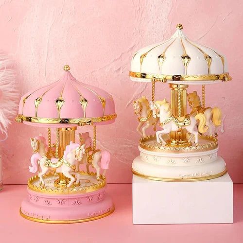 Deux boîtes à musique carrousel. Une rose pâle avec des chevaux blancs et une blanche avec des chevaux dorés.