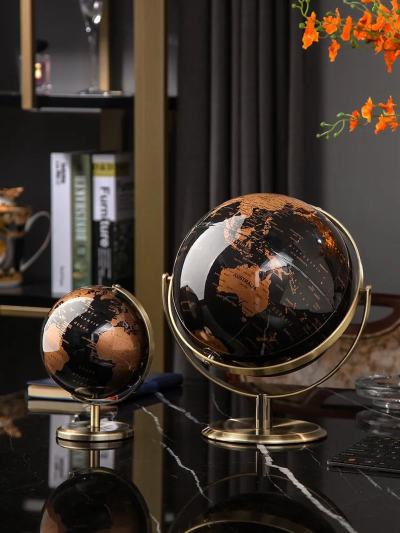Deux globes terrestres décoratifs en plastique noir et cuivre avec support en métal doré, sur une table noire.