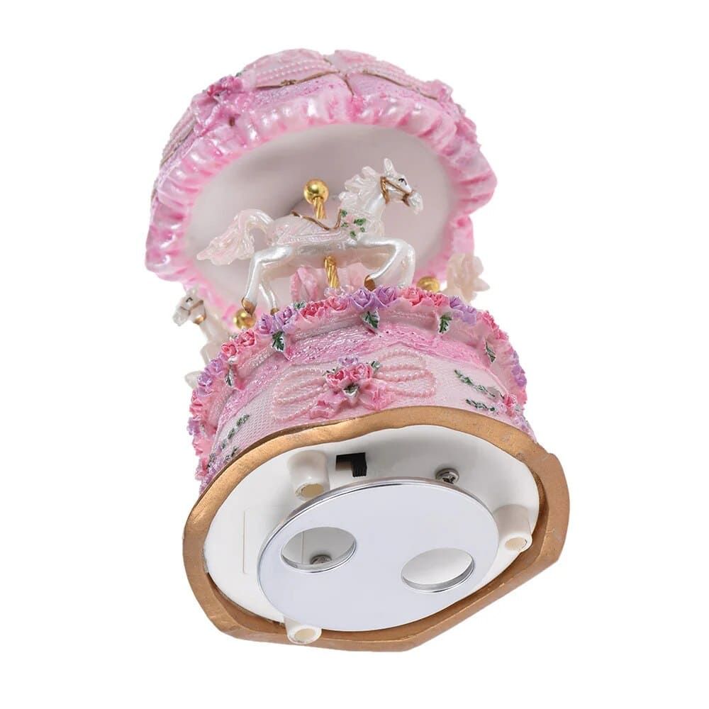 Boîte à musique carrousel rose avec trois chevaux blancs sous un auvent, décorée de fleurs.