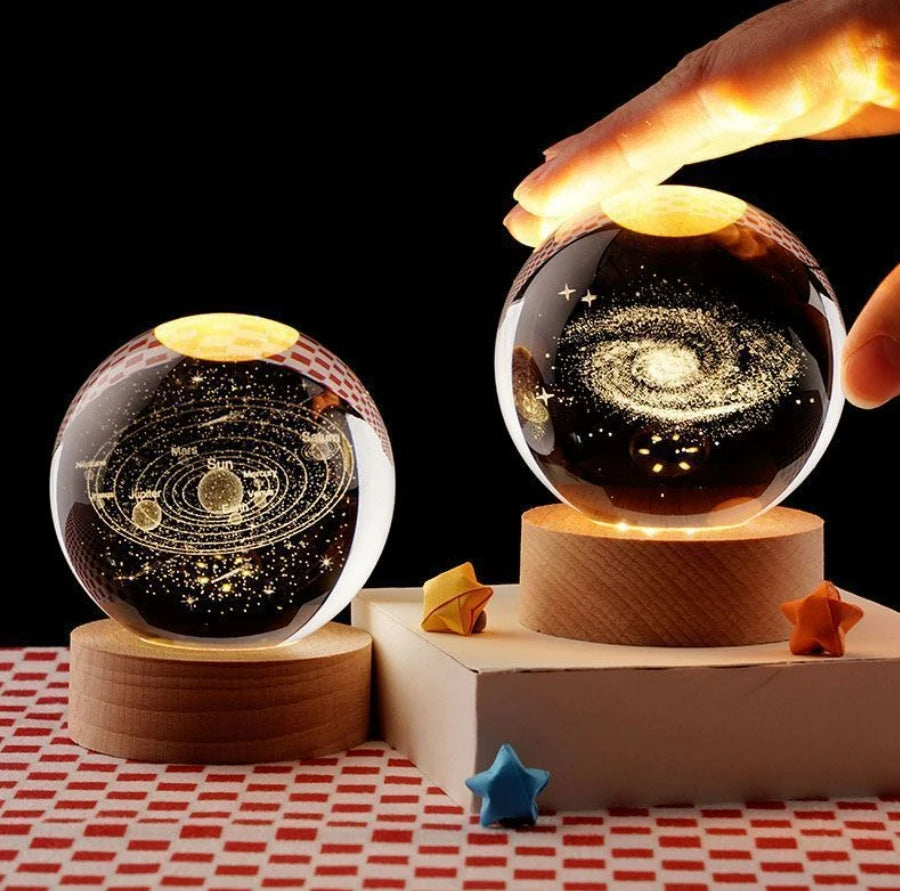 Deux veilleuses LED en sphères de verre de 6 cm, sur des bases en bois. L'une représente une galaxie, l'autre le système sola