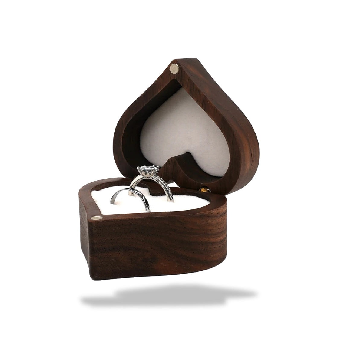 Boîte à bijoux en forme de cœur en bois de noyer foncé ouverte, contenant deux bagues argentées sur un coussin blanc.