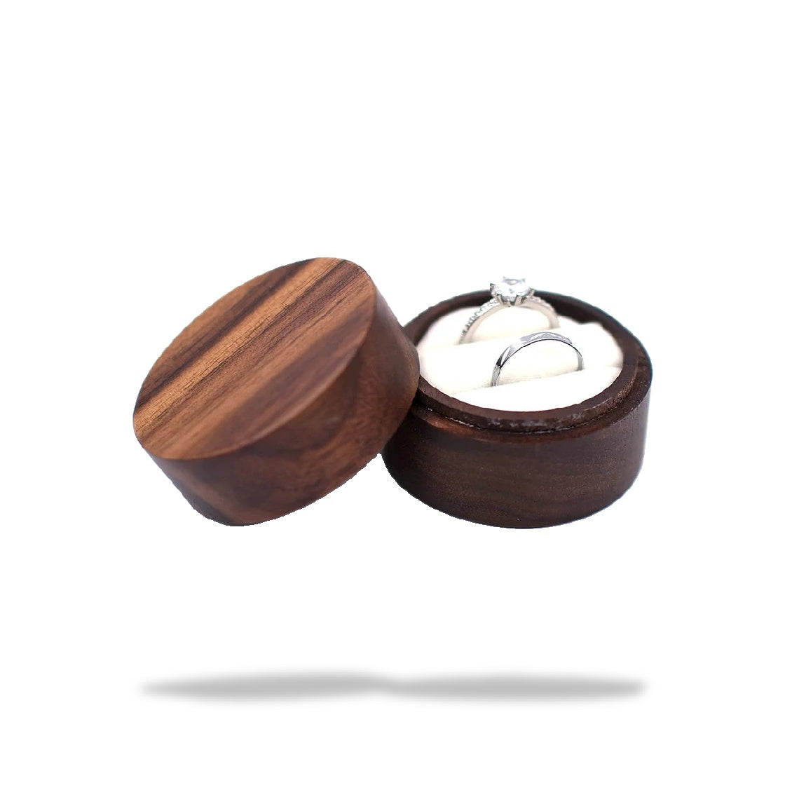 Boîte à bague de fiançailles ronde en bois sombre, ouverte. Un coussinet blanc contient deux bagues en argent.