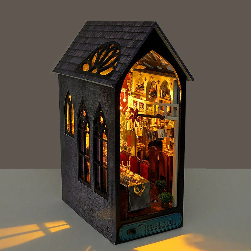 Book nook en forme de restaurant miniature éclairé. Fenêtres gothiques et intérieur détaillé avec tables et chaises.