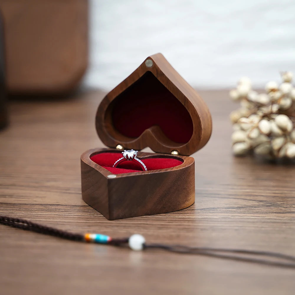 Boîte à bijoux en bois de noyer en forme de cœur ouverte, avec doublure rouge et une bague argentée.