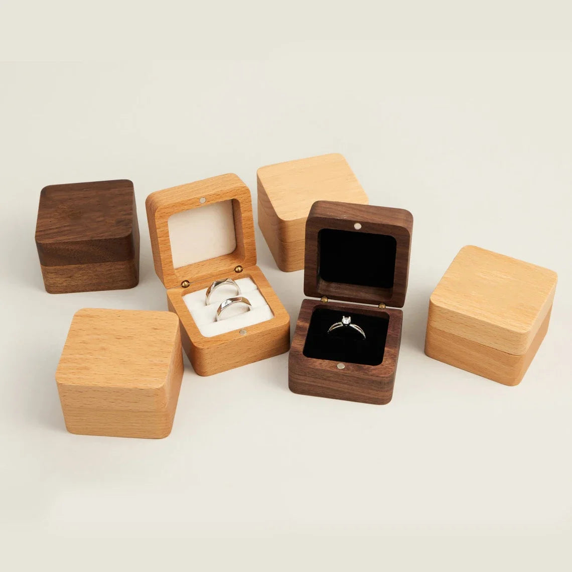 Boîtes à bagues carrées en bois claires et foncées, certaines ouvertes avec des anneaux et un écrin. L'intérieur est en tissu