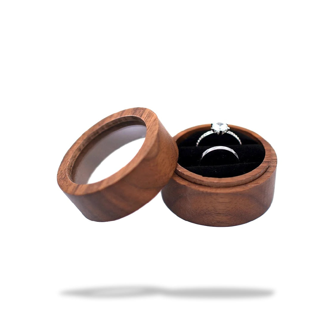 Boîte à bague de fiançailles ronde en bois marron ouverte, avec deux bagues sur un support en tissu noir.