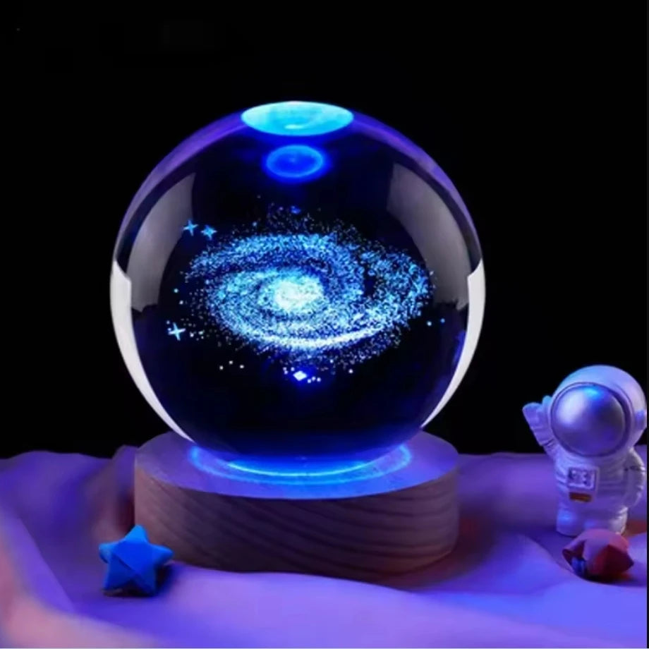 Veilleuse LED avec sphère en verre transparent sur une base en bois, illuminant une galaxie en spirale bleue.