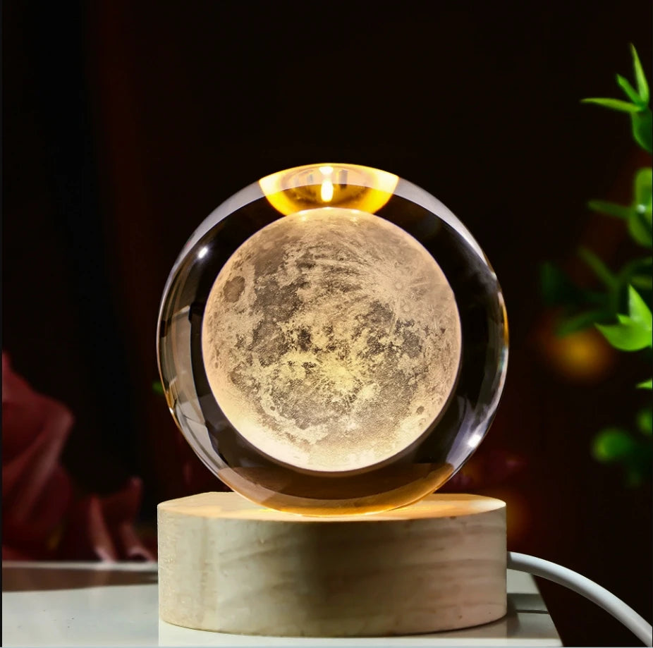 Veilleuse LED avec sphère en verre transparent, motif de lune grise éclairée, posée sur une base en bois.