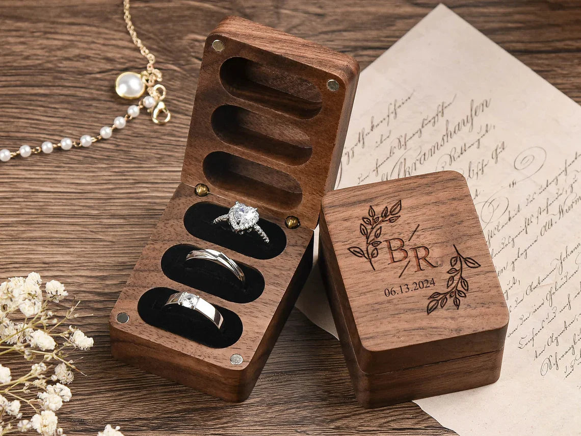 Boîte à bagues en bois de noyer foncé, ouverte et fermée, avec trois emplacements doublés de velours noir. La boîte fermée es