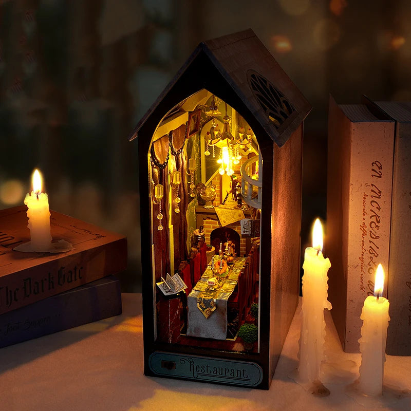 Kit de serre-livres en bois représentant un restaurant miniature, avec lumière LED allumée, posé entre des livres et des boug