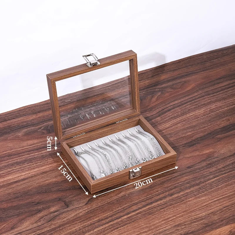 Boîte à bijoux rectangulaire en bois de noyer marron avec couvercle en verre, contenant plusieurs bracelets argentés. Dimensi