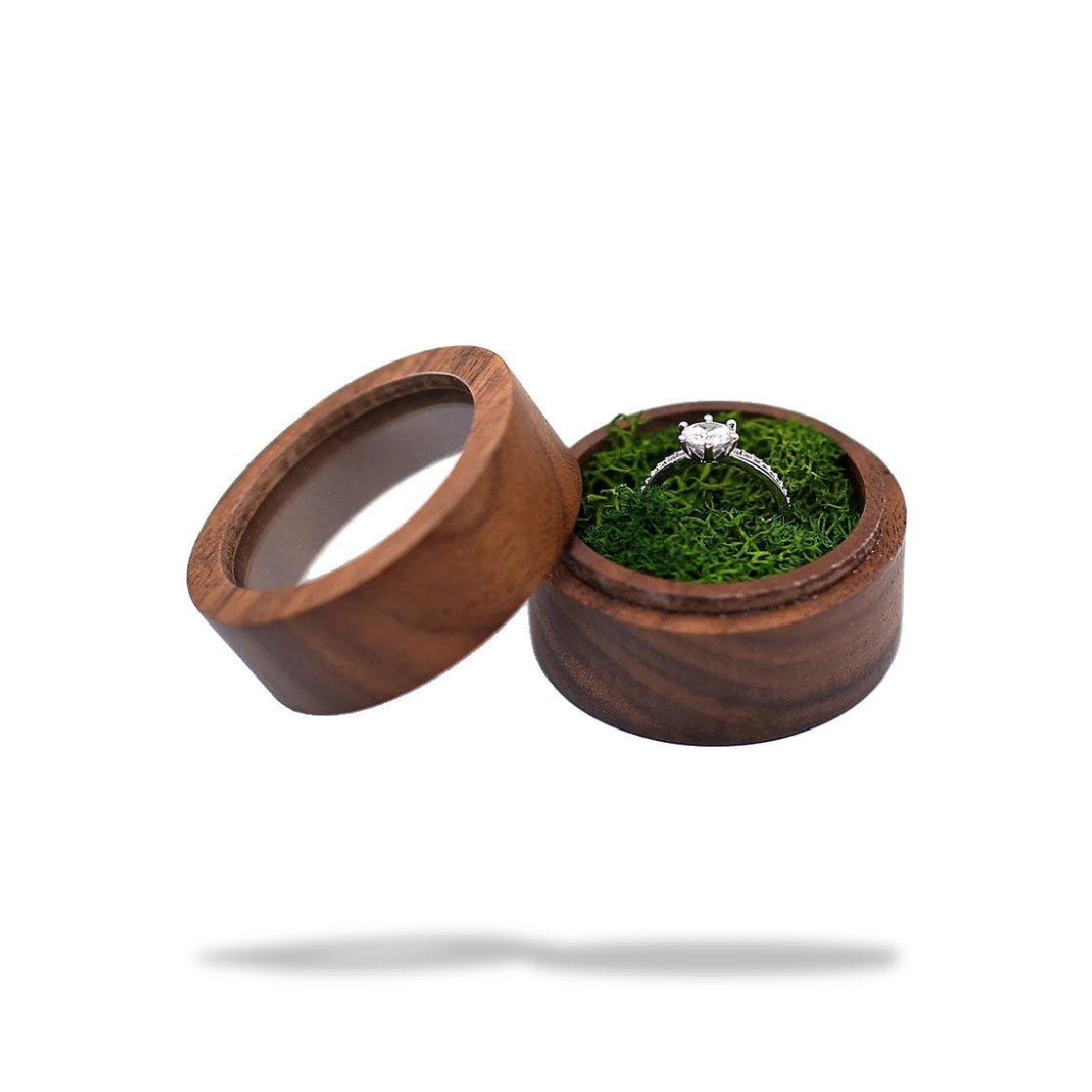 Boîte à bague de fiançailles ronde en bois avec couvercle transparent, contenant une bague argentée sur de la mousse verte.