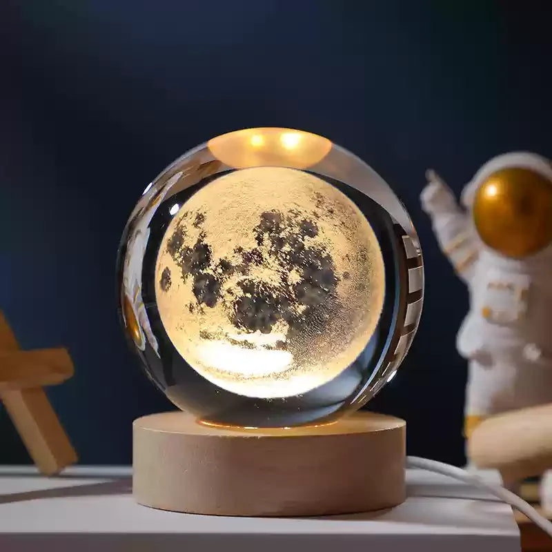 Veilleuse LED avec une sphère en verre transparente de 6 cm affichant la lune illuminée, posée sur une base ronde en bois mas