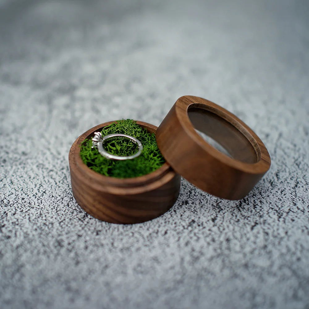 Boîte à bague de fiançailles ronde en bois avec couvercle séparé, intérieur en mousse verte tenant une bague en argent.