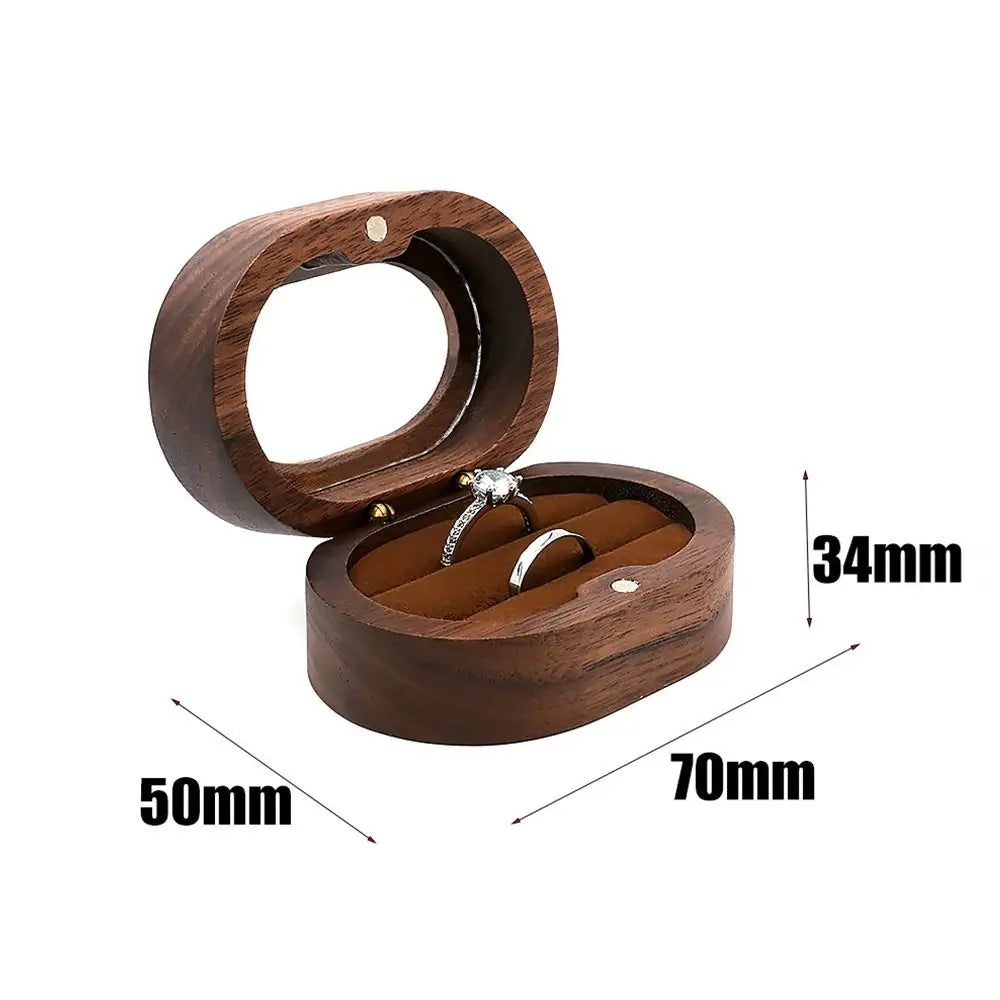 Boîte à bijoux ovale en bois brun, ouverte, avec intérieur en velours marron et deux bagues. Dimensions indiquées : 70mm x 50