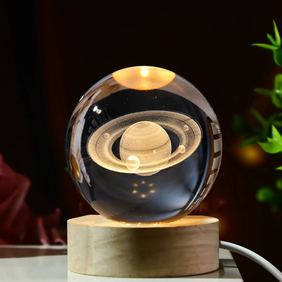 Veilleuse LED avec une sphère en verre abritant une représentation gravée de la planète Saturne, posée sur une base en bois c