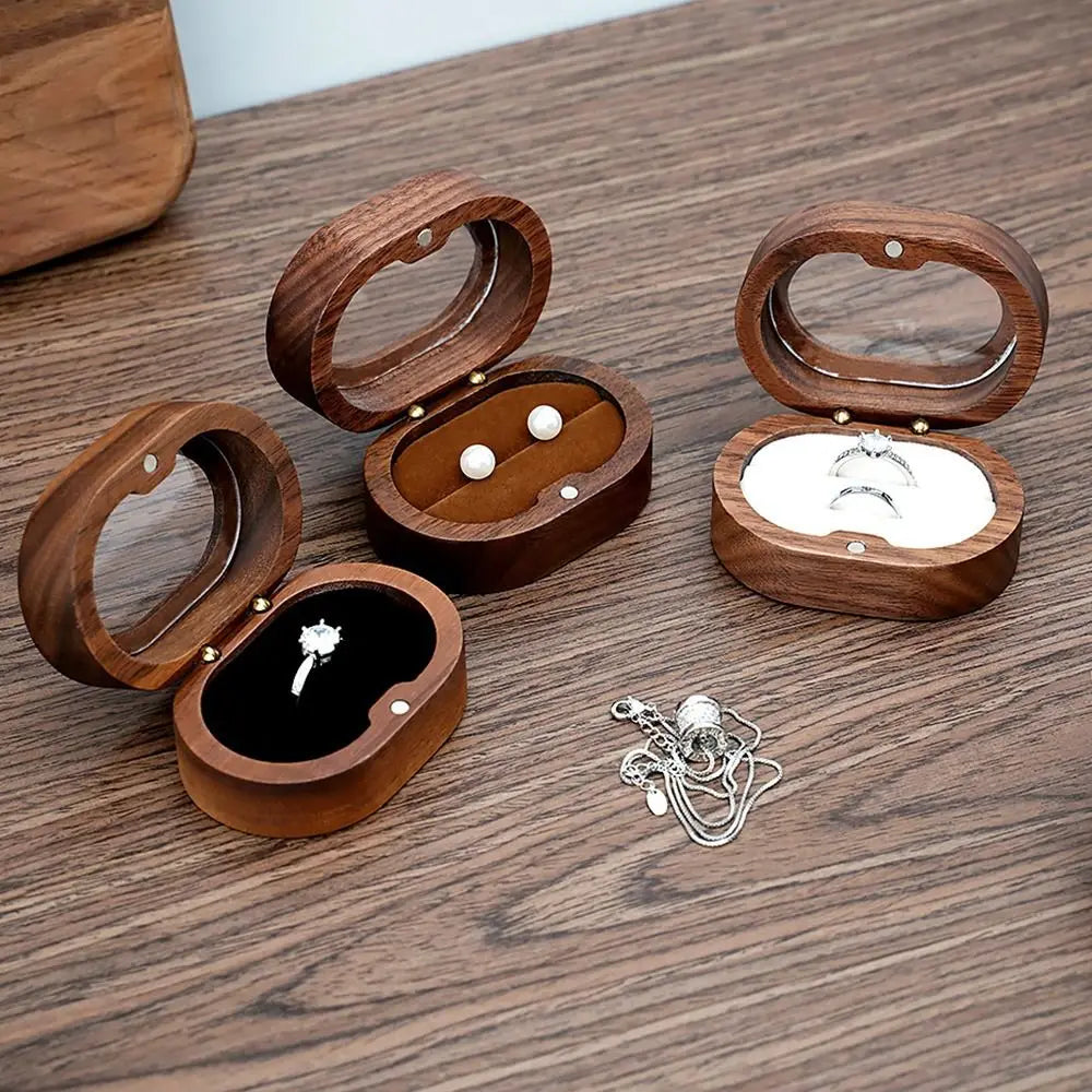 Trois boîtes à bijoux ovales en bois ouvertes sur une table, avec des bijoux à l'intérieur.