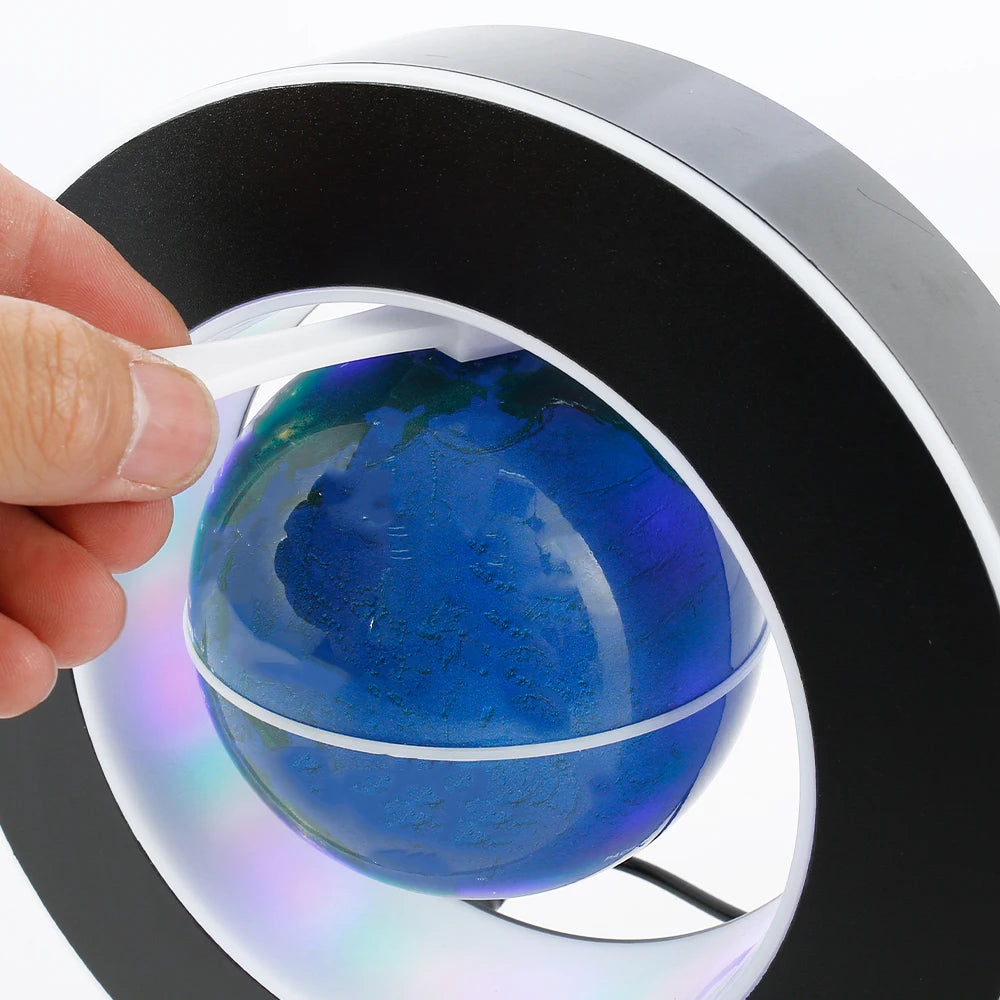 Main ajustant un globe terrestre bleu à lévitation magnétique dans une base noire circulaire, avec reflets lumineux.
