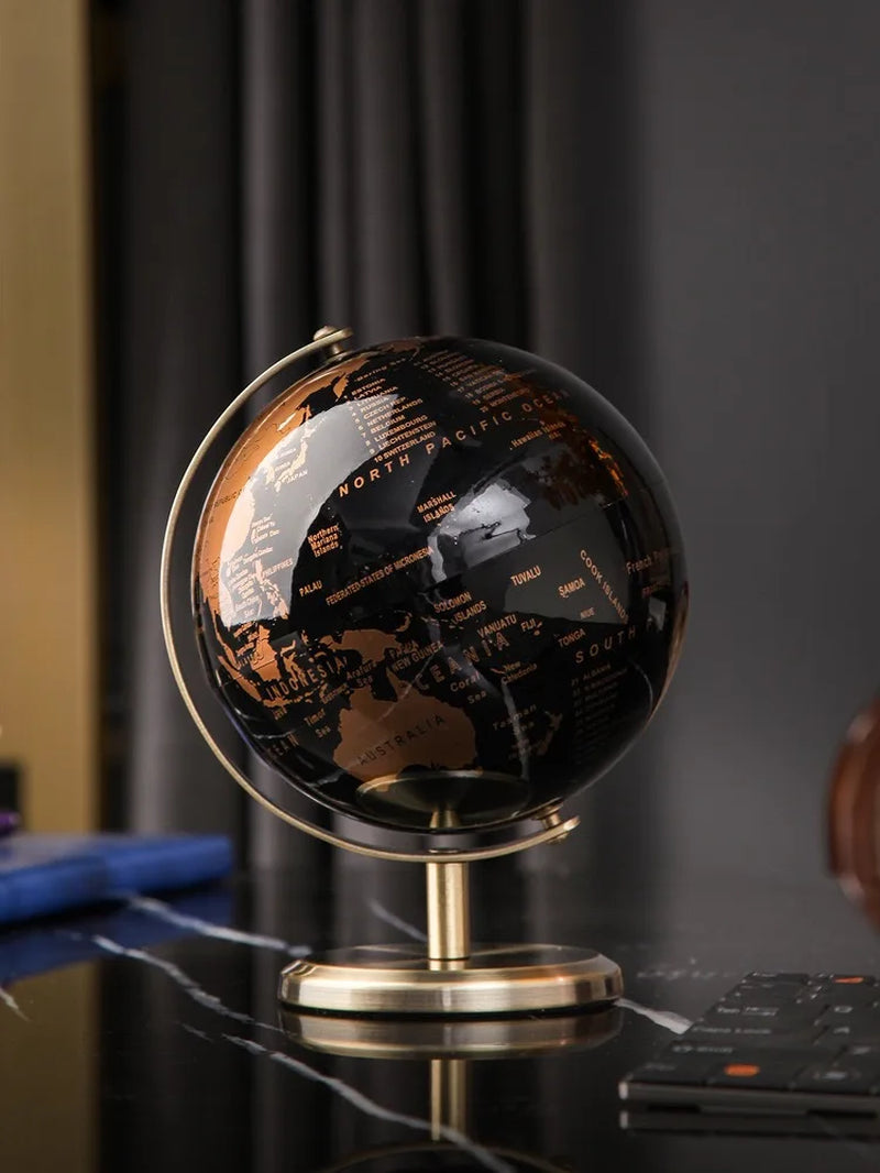 Globe terrestre décoratif avec un planisphère noir et les continents en or brillant, posé sur un support métallique doré.