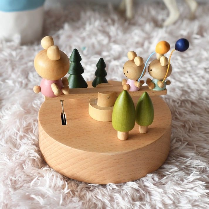 Boîte à musique en hêtre, décorée de lapins et d'arbres miniatures verts, avec deux lapins sur une balançoire.