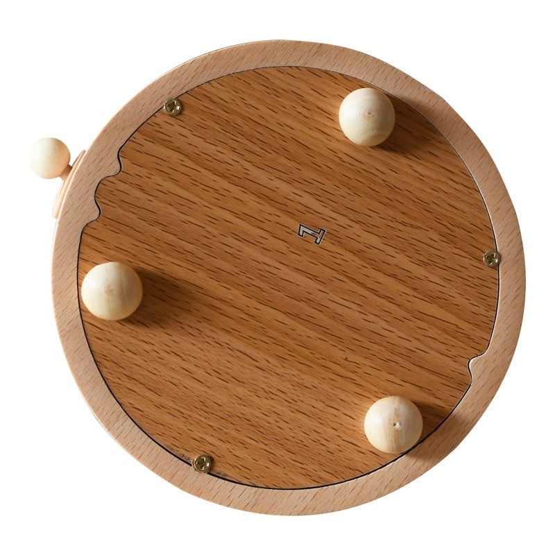 Vue du dessous d'une boîte à musique ronde en bois de hêtre clair. Le fond présente un grain de bois distinct et quatre pieds