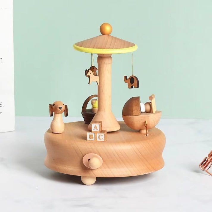 Boîte à musique carrousel enfant en bois clair. Elle présente un chien, un berceau avec bébé et des animaux suspendus.
