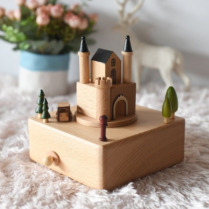 Boîte à musique en hêtre, représentant un château avec des tours et une maison, entourée d'arbres miniatures.
