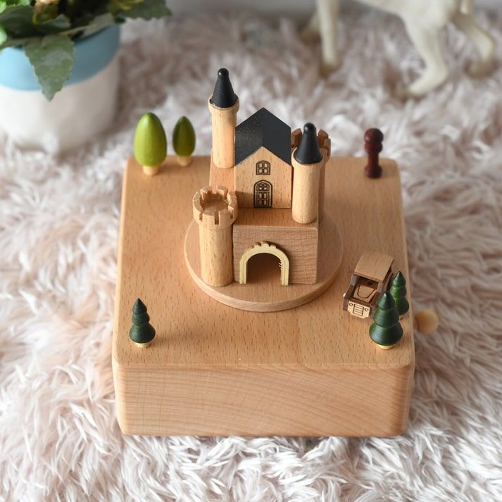 Boîte à musique en bois de hêtre représentant un château avec des tourelles, une voiture et des arbres.