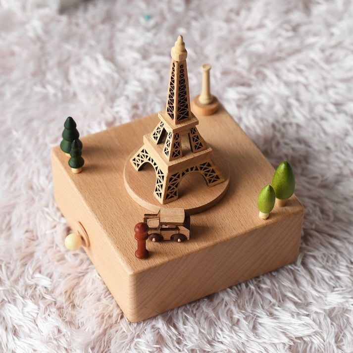Boîte à musique en bois de hêtre, avec Tour Eiffel gravée, petite voiture et arbres miniatures. Fond texturé.