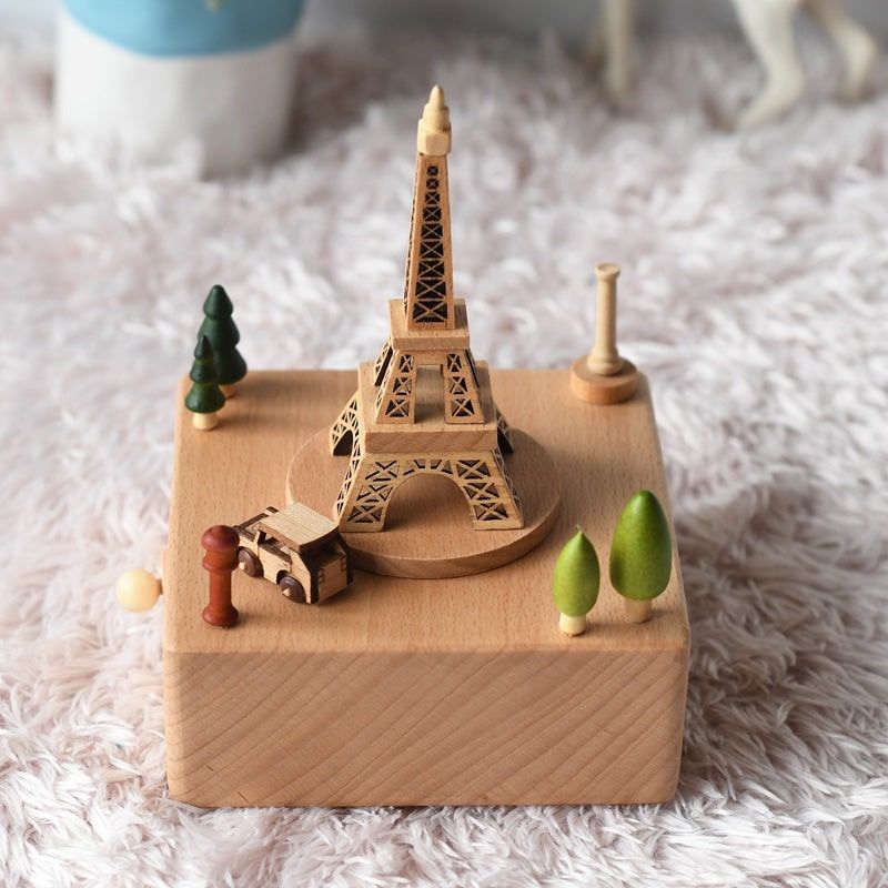 Boîte à musique en hêtre, représentant une Tour Eiffel et des éléments urbains et naturels en bois, sur un socle rectangulair