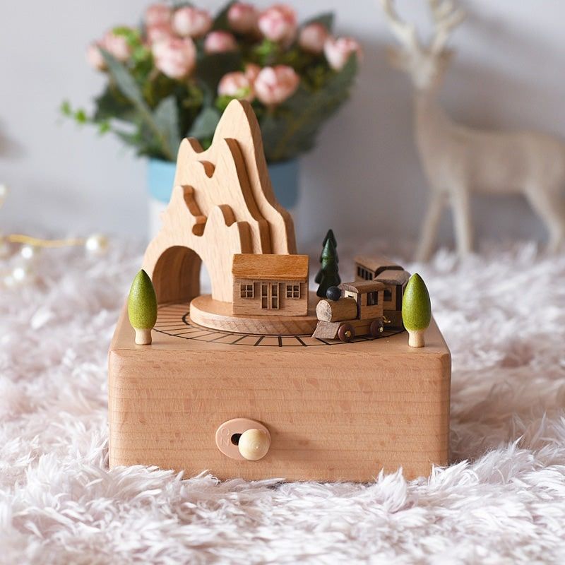 Boîte à musique en bois de hêtre, représente une maison, des arbres et un train en rotation devant une montagne.