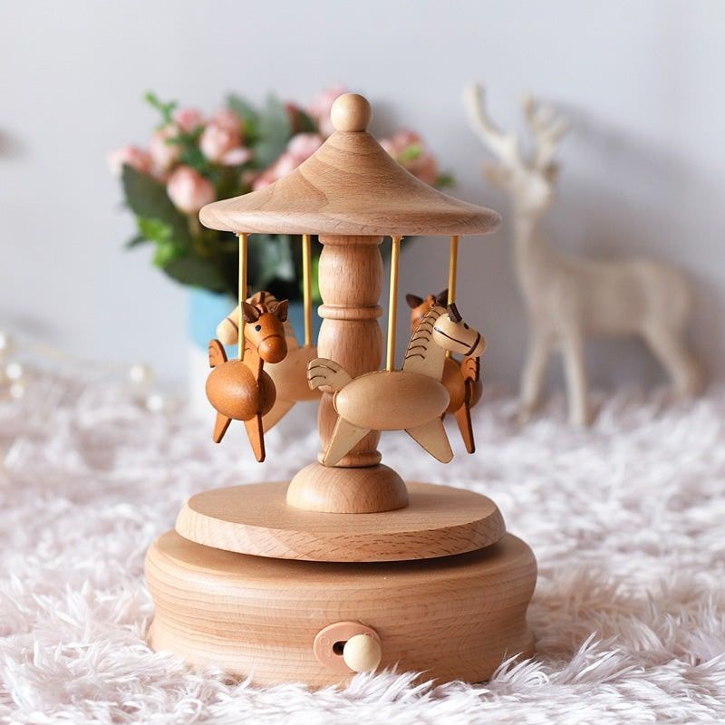 Boîte à musique manège avec trois chevaux en hêtre clair, sur une base ronde avec un remontoir visible.