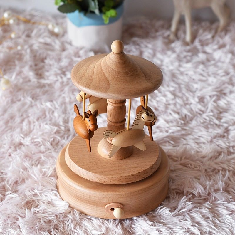 Boîte à musique en bois de hêtre naturel, forme manège avec chevaux sculptés, posée sur un tapis clair.