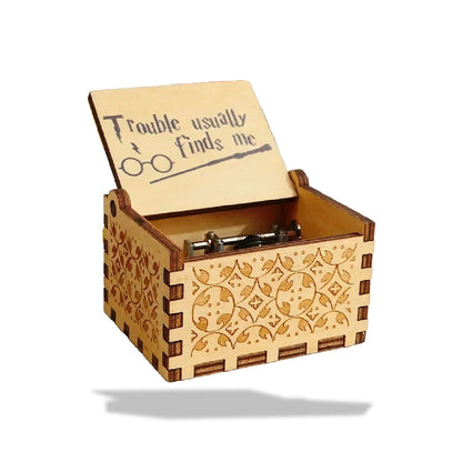 Boîte à musique en bois clair avec motifs floraux gravés. Le couvercle ouvert affiche une inscription Harry Potter.