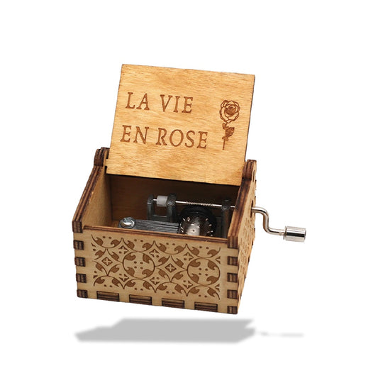 Boîte à musique en bois clair avec un couvercle ouvert affichant 'LA VIE EN ROSE' et une rose gravée.