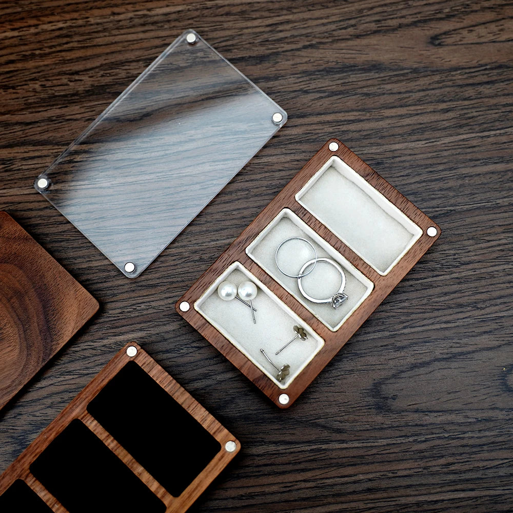 Boîte à bijoux en bois marron foncé avec couvercle transparent, présentant trois compartiments intérieurs en velours blanc. D