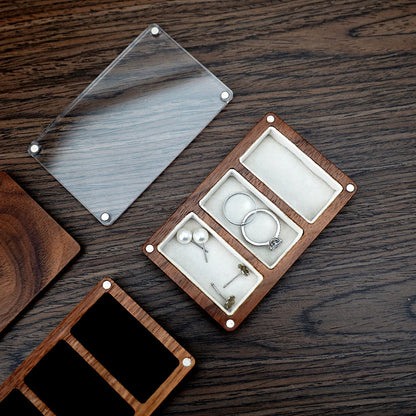Boîte à bijoux en bois marron foncé avec couvercle transparent, présentant trois compartiments intérieurs en velours blanc. D