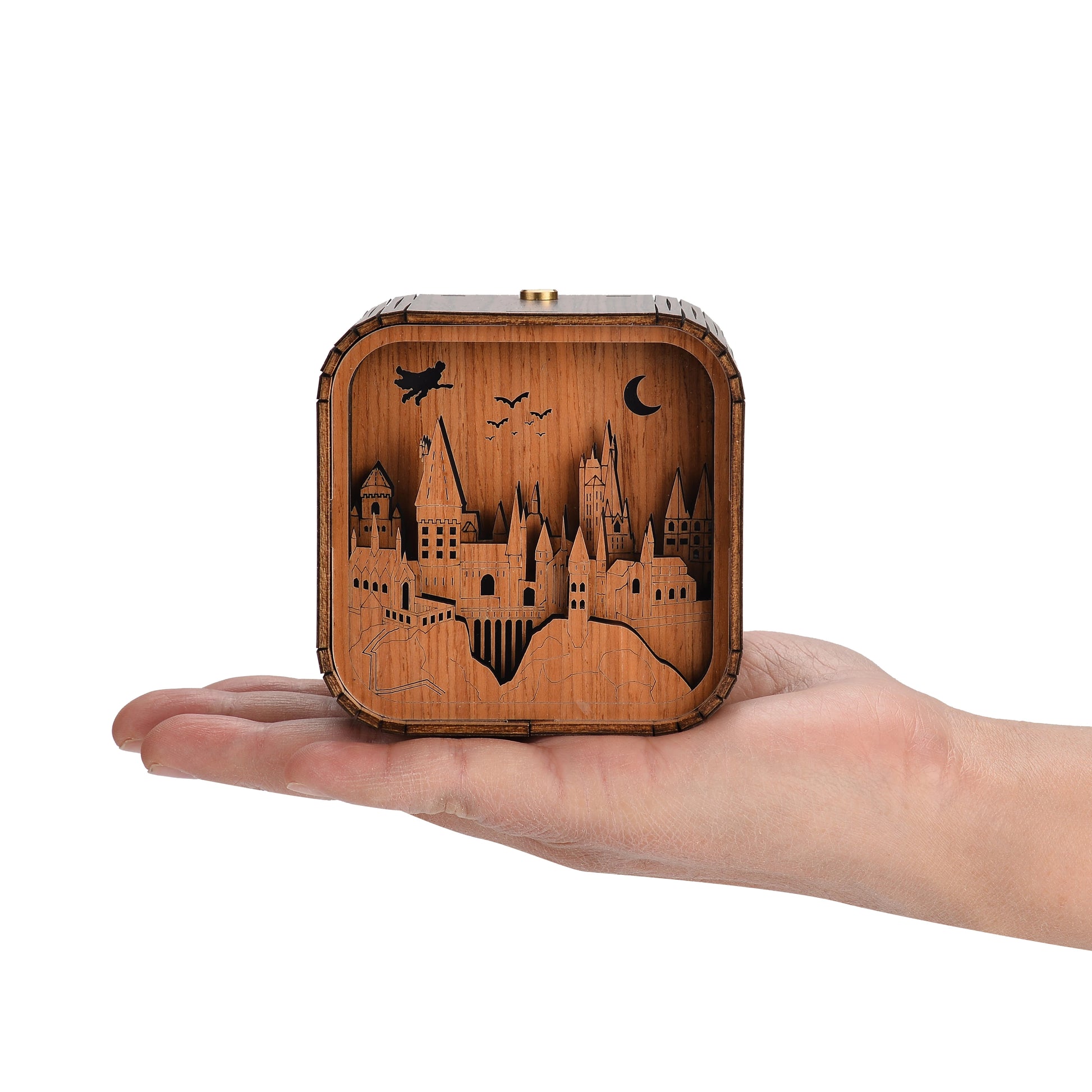 Boîte à musique veilleuse en bois, tenue dans une main, avec un décor découpé de château et un personnage volant.