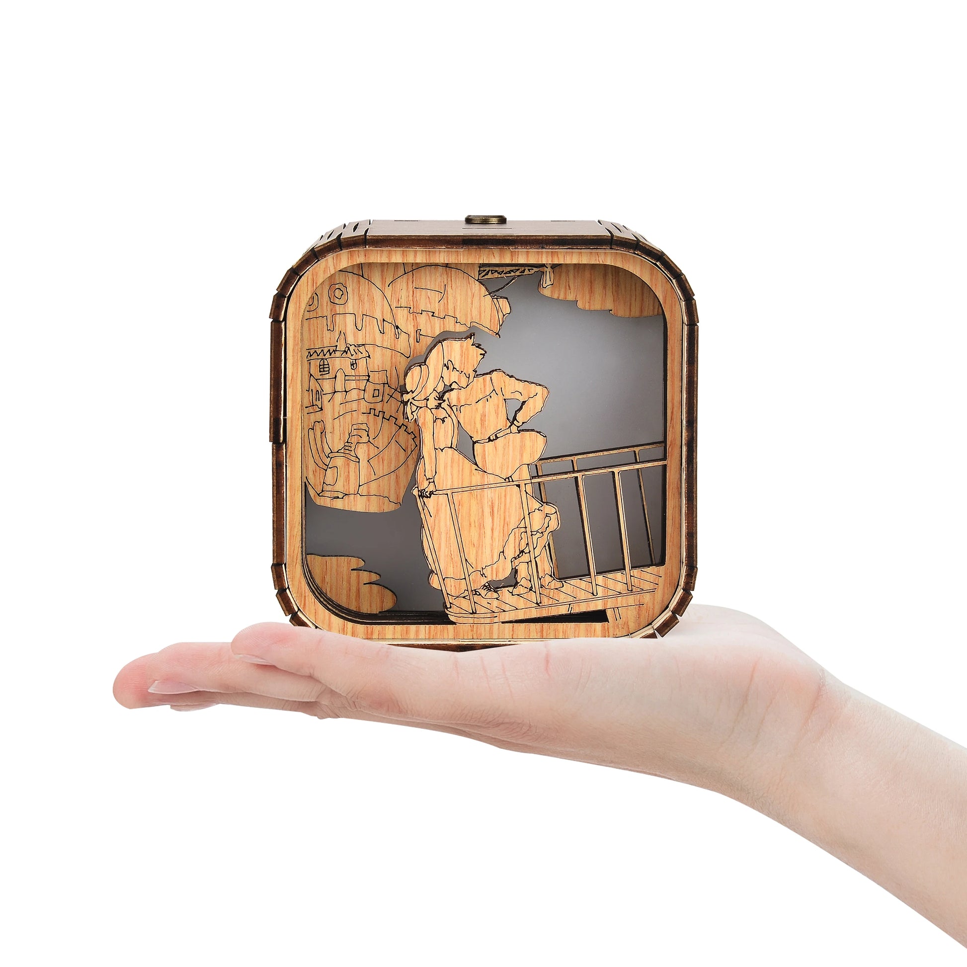 Boîte à musique veilleuse rectangulaire en bois, design gravé d'un couple et d'un bâtiment sur un fond sombre. Tenue par une