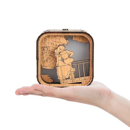 Boîte à musique veilleuse rectangulaire en bois, design gravé d'un couple et d'un bâtiment sur un fond sombre. Tenue par une