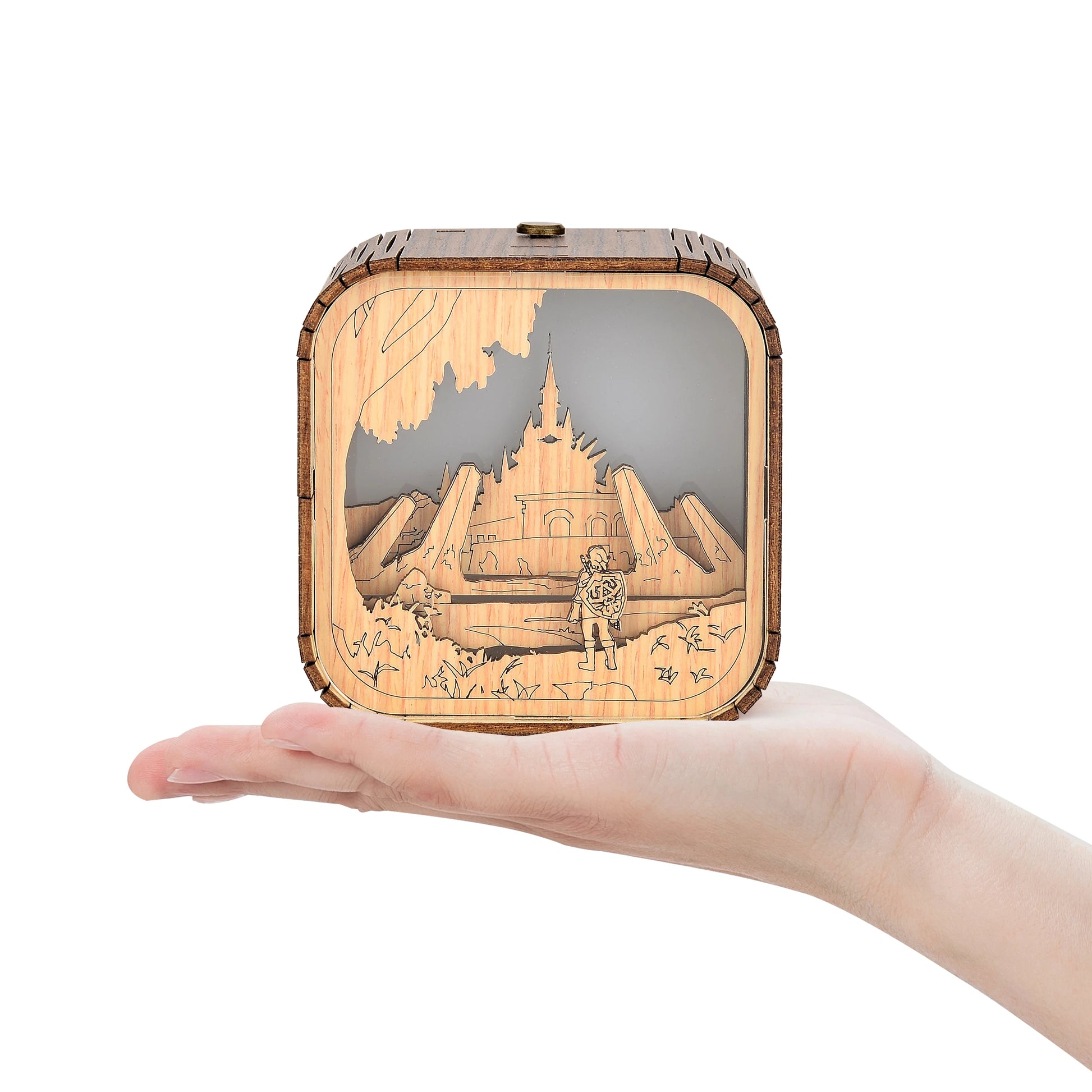 Boîte à musique veilleuse en bois, tenue dans une main, avec un décor découpé au laser d'un château et d'un personnage.