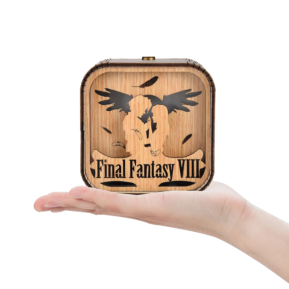 Boîte à musique en bois clair posée dans une main, avec un motif gravé Final Fantasy VIII et des anges