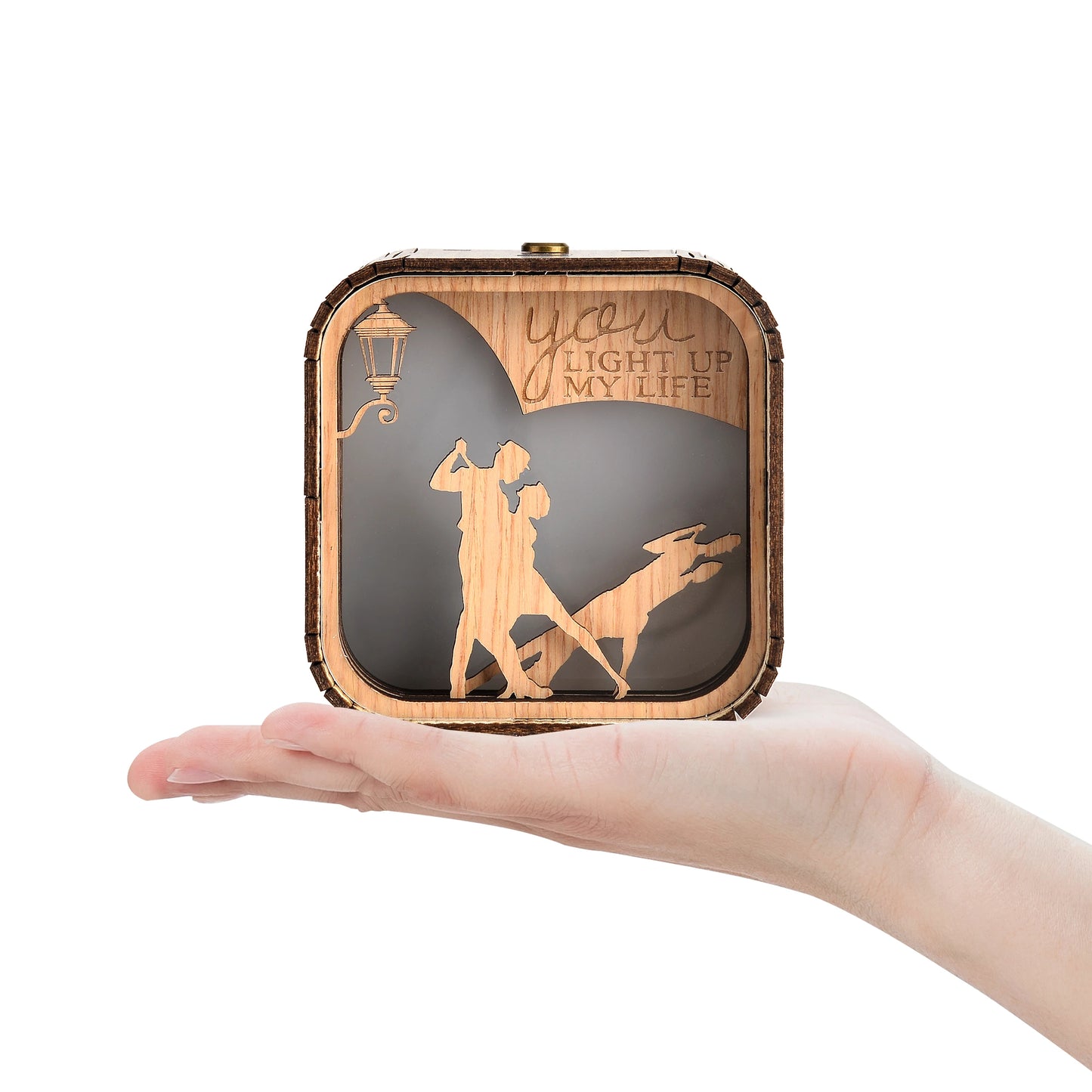 Boîte à musique veilleuse en bois, tenue dans une main, avec scène de danseurs et réverbère. Texte "You Light Up My Life" vis