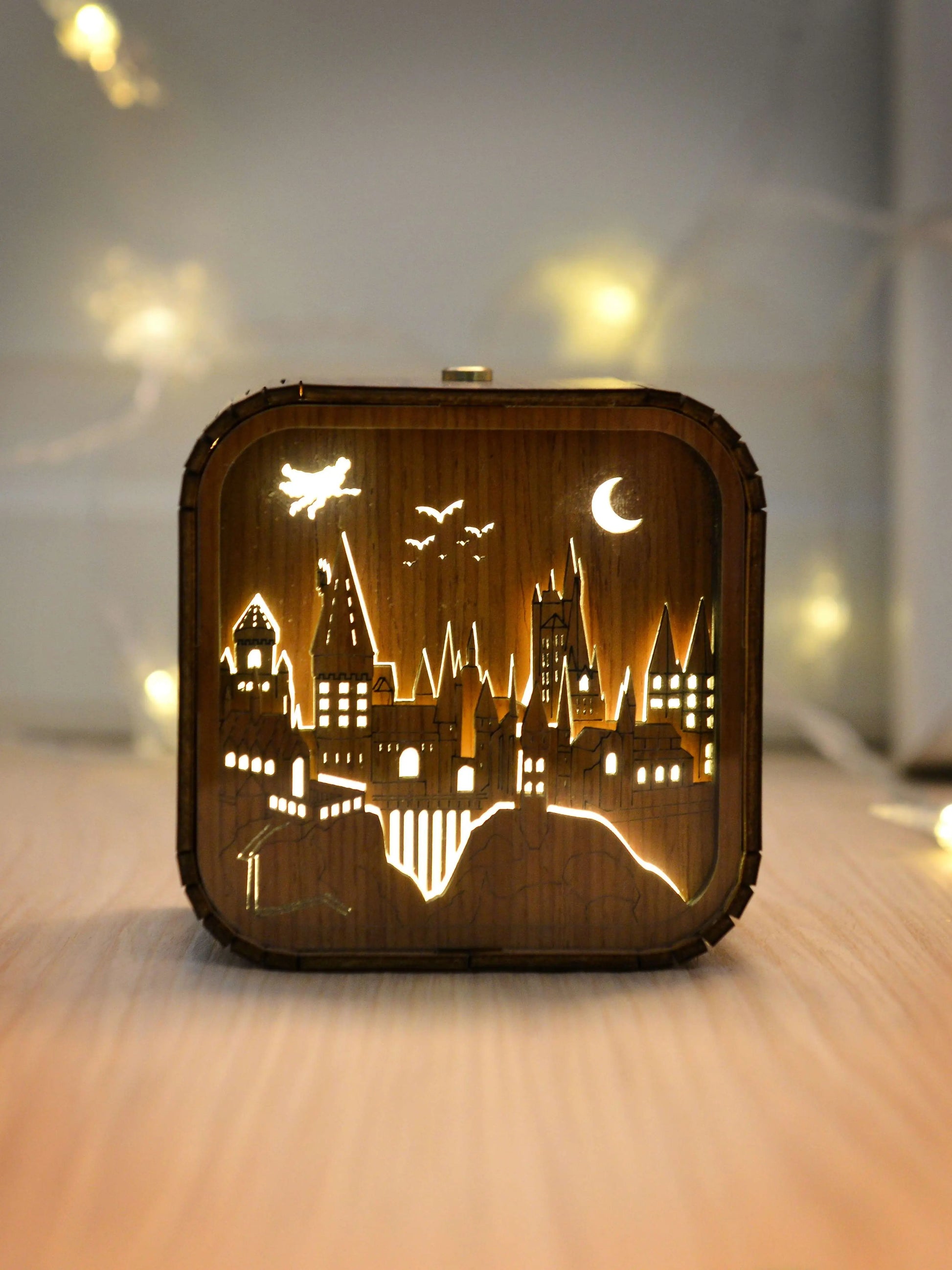Boîte à musique veilleuse en bois, château éclairé avec lune et chauves-souris, posée sur une table.