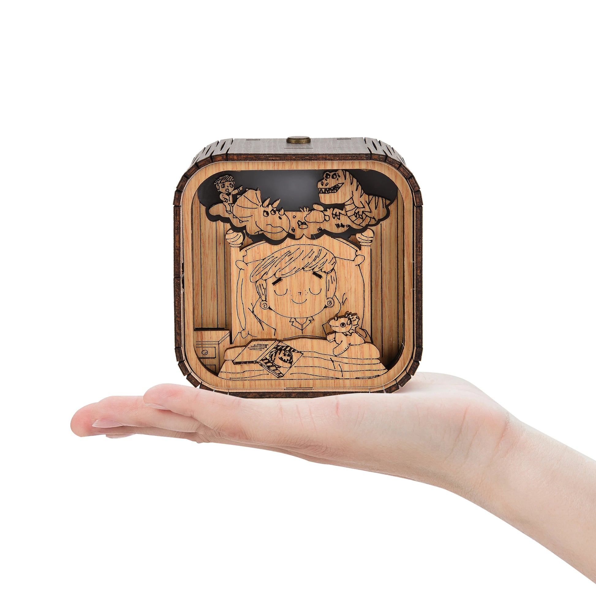 Boîte à musique veilleuse en bois, tenue dans une main, avec une scène d'enfant endormi et des dinosaures.