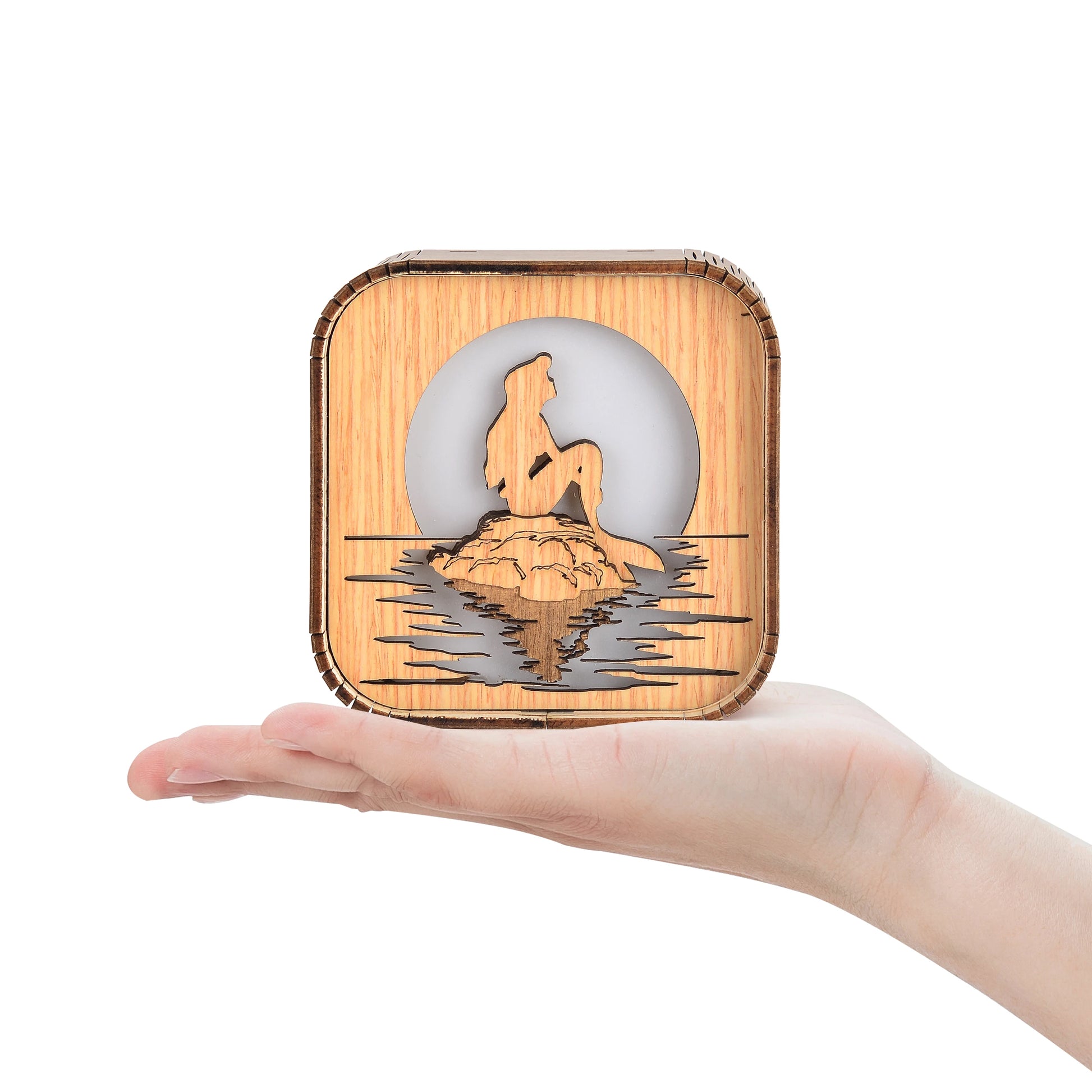 Boîte à musique veilleuse en bois, sur une main, avec silhouette de sirène assise sur un rocher et lune.