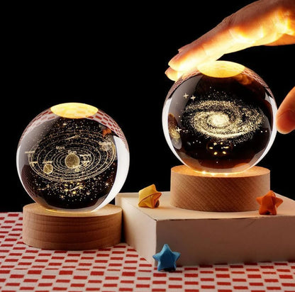 Deux veilleuses LED en sphères de verre de 6 cm, sur des bases en bois. L'une représente une galaxie, l'autre le système sola