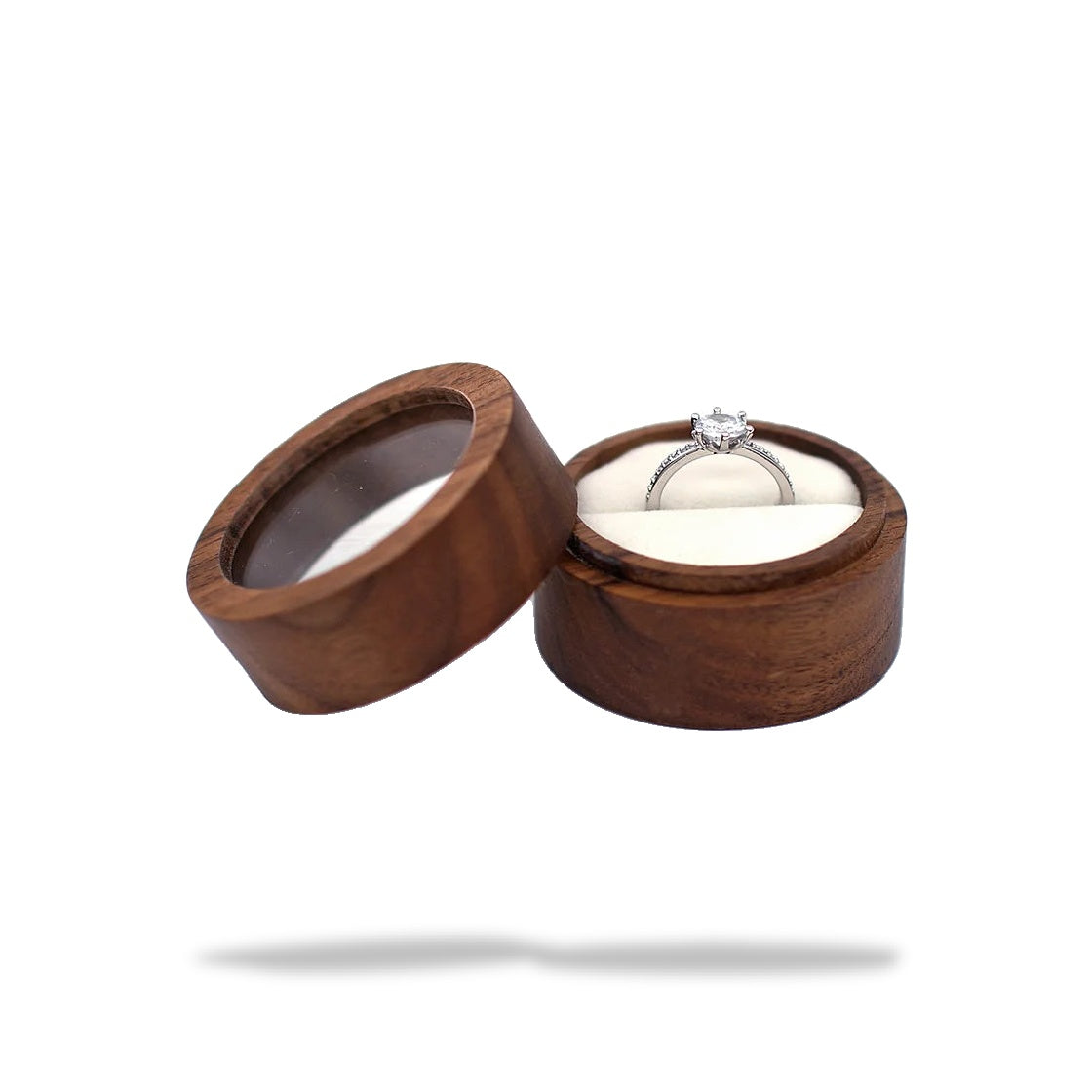 Boîte à bague de fiançailles ronde en bois, ouverte, avec une bague en argent et diamant sur un support blanc.