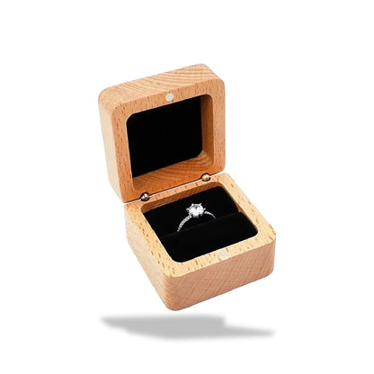 Boîte à bagues en bois clair, ouverte, sur fond blanc. Un anneau en argent avec un diamant repose sur un intérieur en velours