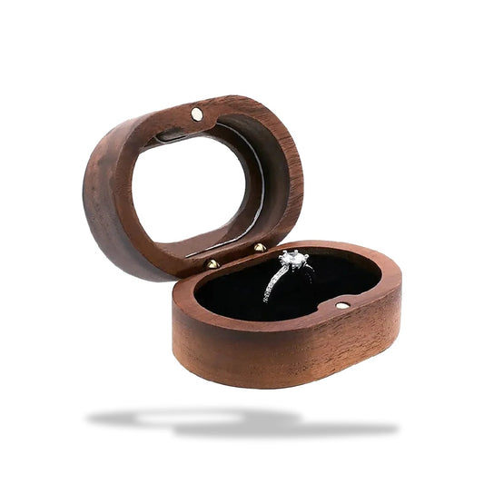 Boîte à bijoux ovale en bois brun, ouverte, avec un anneau orné d'un diamant posé sur un intérieur noir en velours.